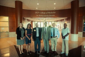 Six people stand in a lobby under a sign that reads UCF College of Medicine Dr. Phillips Charities Rotunda. The group poses for a formal photo.