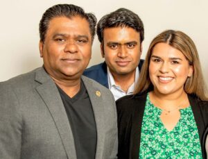 Three people are posing together and smiling for a group photo against a light background.