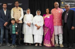 A group of eight adults and one child pose for a photo in front of banners for the College of Sciences and The India Center at UCF.