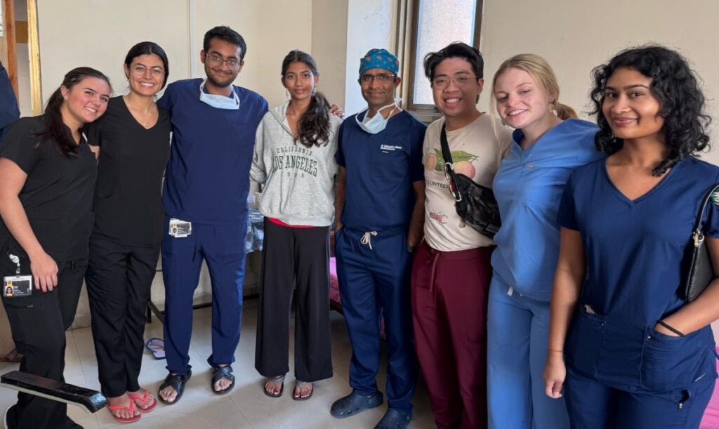 A group of seven people in medical attire stand indoors, smiling and posing for a group photo.