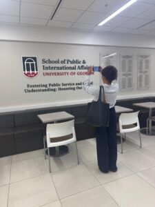 A woman stands taking a photo of a wall at the University of Georgia’s School of Public & International Affairs, next to tables and chairs in a hallway.