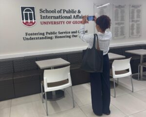 A woman stands taking a photo of a wall at the University of Georgia’s School of Public & International Affairs, next to tables and chairs in a hallway.