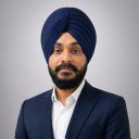 A man wearing a navy blue turban and suit jacket over a white shirt poses against a plain gray background.