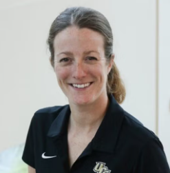 A woman smiling and wearing a black polo shirt with a university logo.